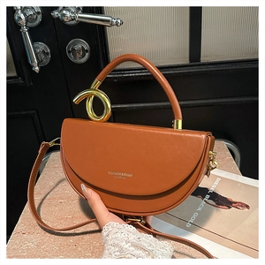Detail of a brown leather half-moon saddle bag with gold hardware and top handle