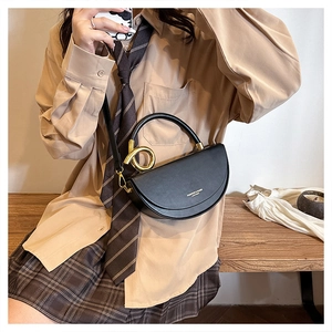 Detail of black saddle bag with round gold metal handle and leather texture finish