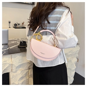 Detail of pink crescent bag featuring a distinctive golden metal circular handle and crossbody strap