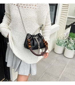 Detail of black leather bucket bag with wooden bead handle and metal tassel decoration