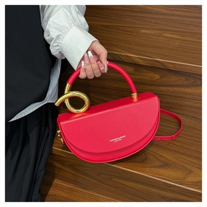 Red leather saddle bag detail with golden circular handle held on wooden stairs