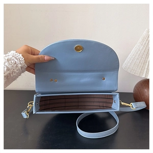 Macro detail of the light blue saddle bag featuring magnetic gold clasp and striped lining