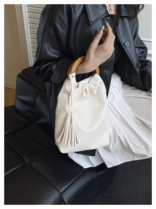 Detalle del bolso de hombro blanco crema con asa redonda de madera y borlas de cuero