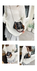 Detail of black PU bucket bag featuring wooden bead handle and silver tassel accessory