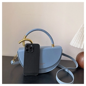 Light blue half-moon saddle bag with gold metal rings beside a smartphone for size reference