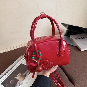 Red glossy leather mini Boston bag with vintage bead pendant and bow on a wooden table
