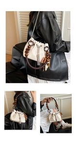 Detail view of cream PU bucket bag featuring wooden bead handle and metal tassel drawstring
