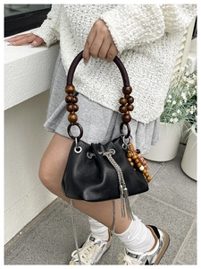 Detail of black leather drawstring bucket bag with vintage wooden bead handle and silver chain