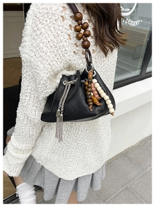 Detail of black drawstring bucket bag featuring wooden bead strap and silver metal tassels
