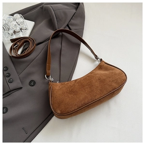 Detalle de bolso hobo de ante marrón con correa ajustable sobre un blazer gris