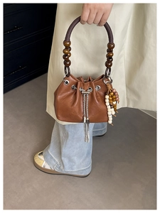Detail of retro brown leather bucket bag with unique wooden bead handle and tassel