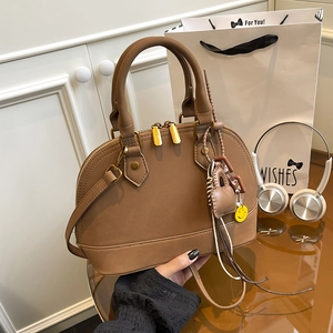 Brown shell-shaped handbag with adjustable strap and smiley charm in a lifestyle setting