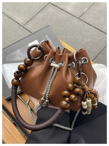 Detailed shot of brown leather bucket bag with wooden bead handle on a wooden bench