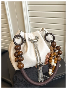 Close-up of white pleated bucket bag with silver tassels and wooden bead handle