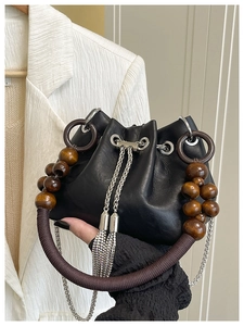 Detail of black leather bucket bag with artistic wooden bead handle and silver chain fringe