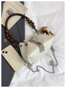 Close-up of cream bucket bag with wooden bead handle and silver tassel detail