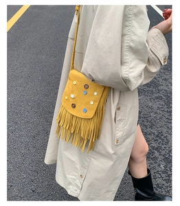 Detail of yellow suede crossbody bag with bohemian tassels and decorative buttons
