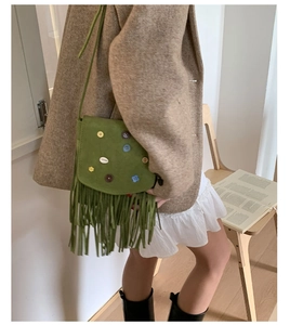 Detail of green suede crossbody bag featuring retro tassels and floral button accents