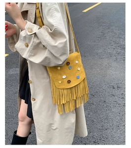 Detail of yellow suede crossbody bag featuring bohemian fringe and colorful button accents