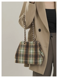 Detail of wool-like plaid bucket bag with gold chain strap worn over a khaki trench coat