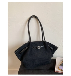 Detail of black matte suede tote bag with leather strap and buckle on a grey cushion
