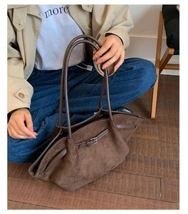 Detail of a large brown suede tote bag featuring a decorative belt buckle and slim handles
