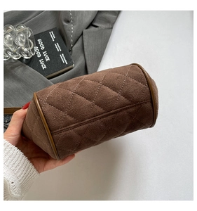 Close-up of brown suede cylinder handbag featuring classic quilted diamond stitching pattern