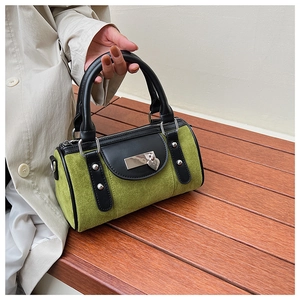Détail du sac Boston en daim vert mousse avec breloque cœur sur un banc en bois