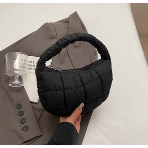 Detail of black quilted cloud bag with thick handle and metal zipper on neutral backdrop