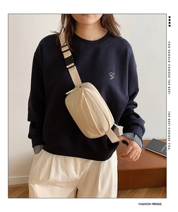 Detail view of a beige nylon crossbody bag with adjustable strap and plastic buckle closure