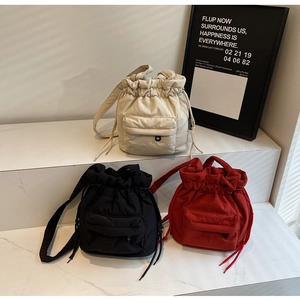 Detail of drawstring nylon crossbody bags in cream, black, and red with front pockets