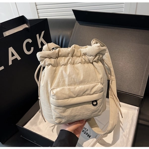 Detail of cream nylon bucket bag with drawstring closure and front zipper pocket in gift box