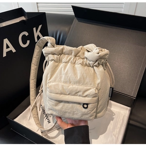 Detail of beige nylon bucket bag with quilted texture, drawstring closure and side logo