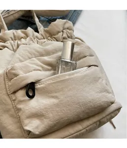 Detail of beige nylon crossbody bag featuring drawstring closure and front zipper pocket