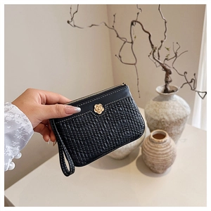 Detail of black woven texture wallet featuring a golden camellia flower and wristlet strap