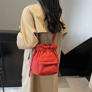 Vibrant red nylon bucket bag with drawstring closure worn with a classic khaki trench coat