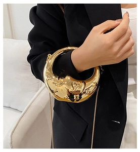 Detailed relief of a sleeping moon face on a shiny gold metallic evening handbag