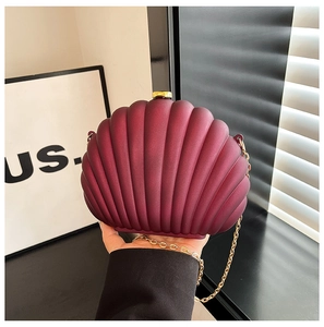 Detail of burgundy shell-shaped clutch with matte texture and gold chain strap