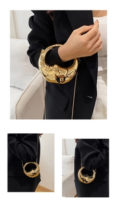 Detail of gold crescent evening bag with surreal face relief and delicate metal chain