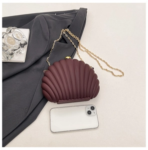 Burgundy shell-shaped clutch bag with gold chain shown next to a smartphone for size reference