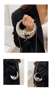 Close-up of a silver crescent-shaped mini bag with moon face relief and metal chain