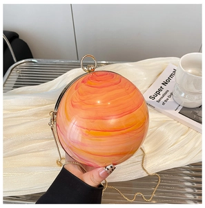 Dettaglio macro della borsa sferica in resina marmorizzata arancione con manico oro