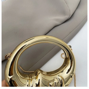 Detailed view of a crescent-shaped gold metal evening bag with circular handle and chain
