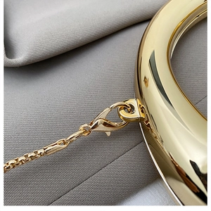 Detail view of the polished gold metallic clasp and chunky chain link on a mini handbag