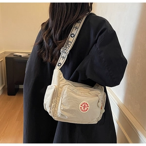 Detail of beige nylon crossbody bag featuring multi-pocket design and wide printed strap