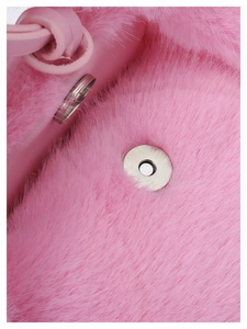 Detail of pink faux fur texture with a round silver magnetic buckle on a fluffy handbag
