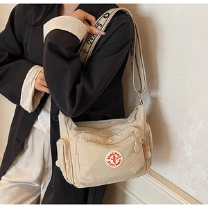 Detailed macro view of a beige nylon crossbody bag with wide floral patterned shoulder strap