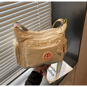 Detail view of a beige nylon crossbody bag with multi-pockets and a colorful woven strap