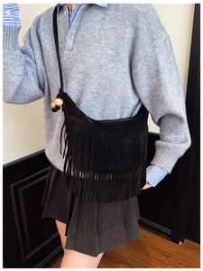 Close-up of black suede tassel crossbody bag with decorative wooden beads on a model