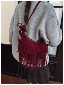 Detail view of deep burgundy suede shoulder bag featuring long fringe and wooden bead accent